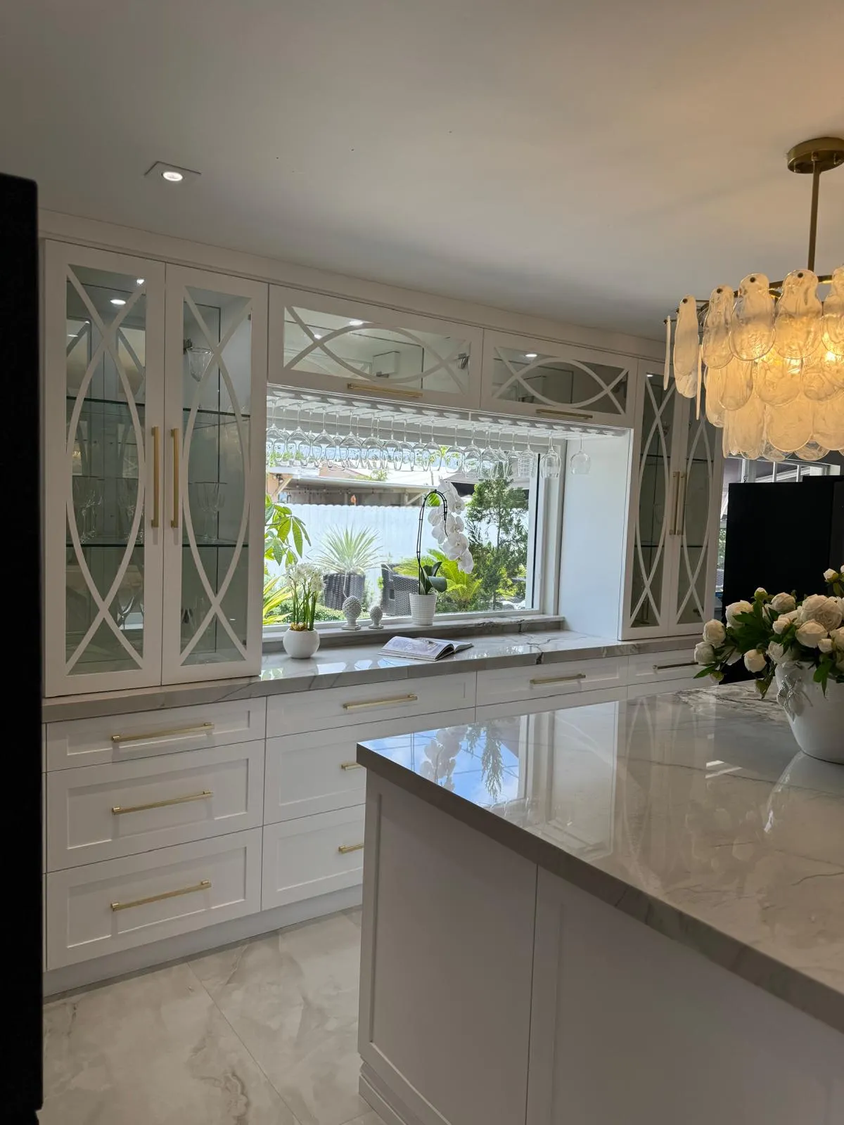 White shaker kitchen with mirrored glass cabinet doors around a garden window and a quartzite island